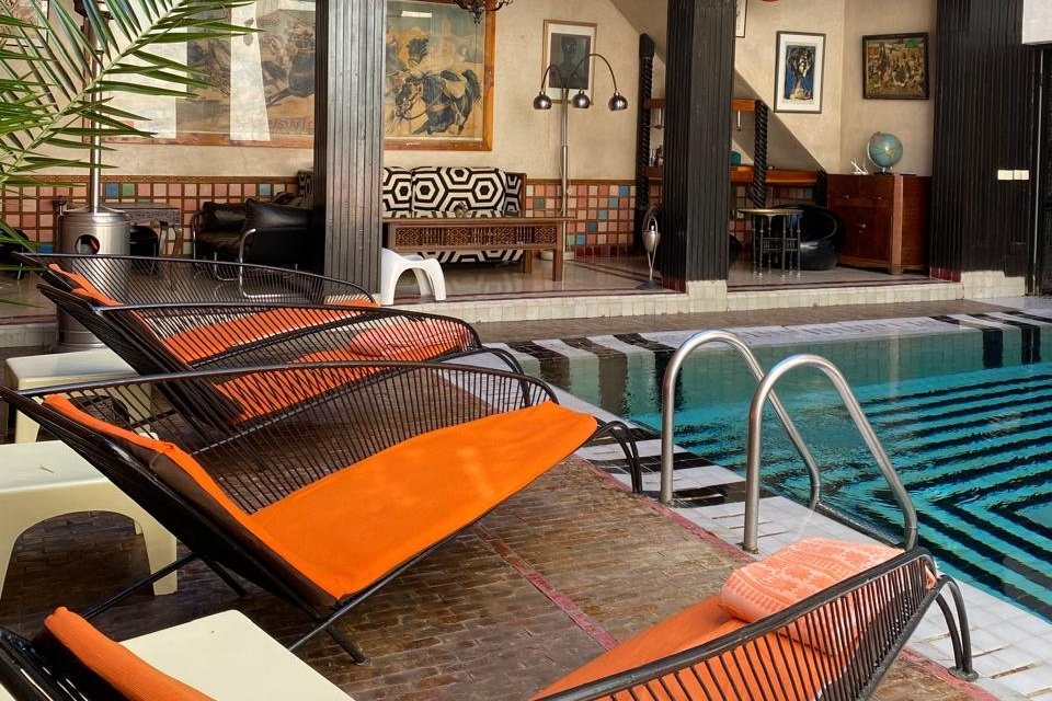 Le patio avec piscine du Riad Malika à Marrakech, avec ses transats orange et sa façade en bois sombre