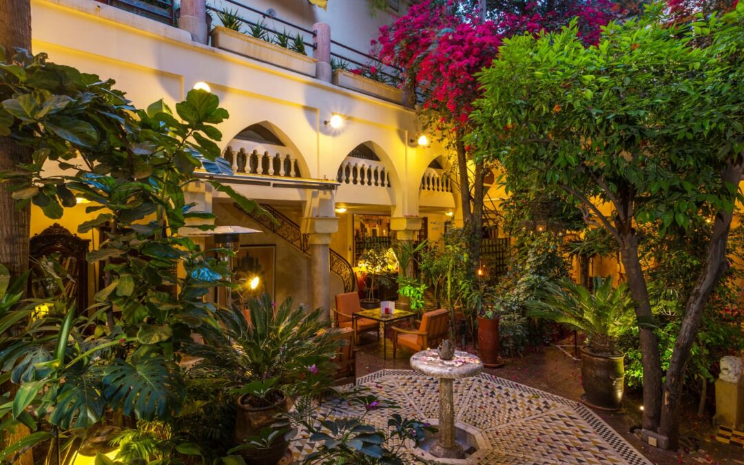 Le patio du Riad Malika à la tombée du jour, avec sa fontaine en zellige, ses arcades éclairées et sa végétation luxuriante